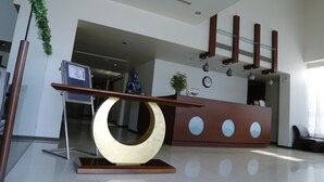 A modern reception area with a wooden reception desk, a large abstract sculpture, and a glass railing. - The Aures (Chhatrapati Sambhajinagar)