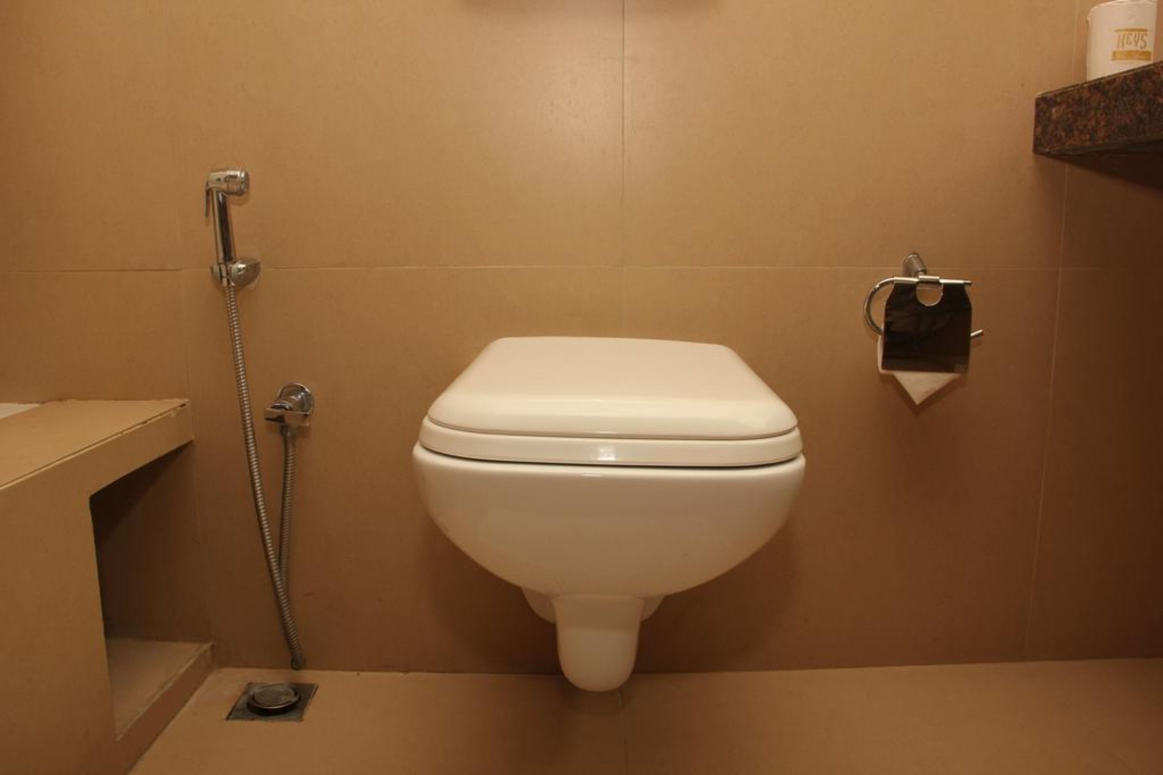 A bathroom with a toilet, a shower, and a shelf with a roll of toilet paper.