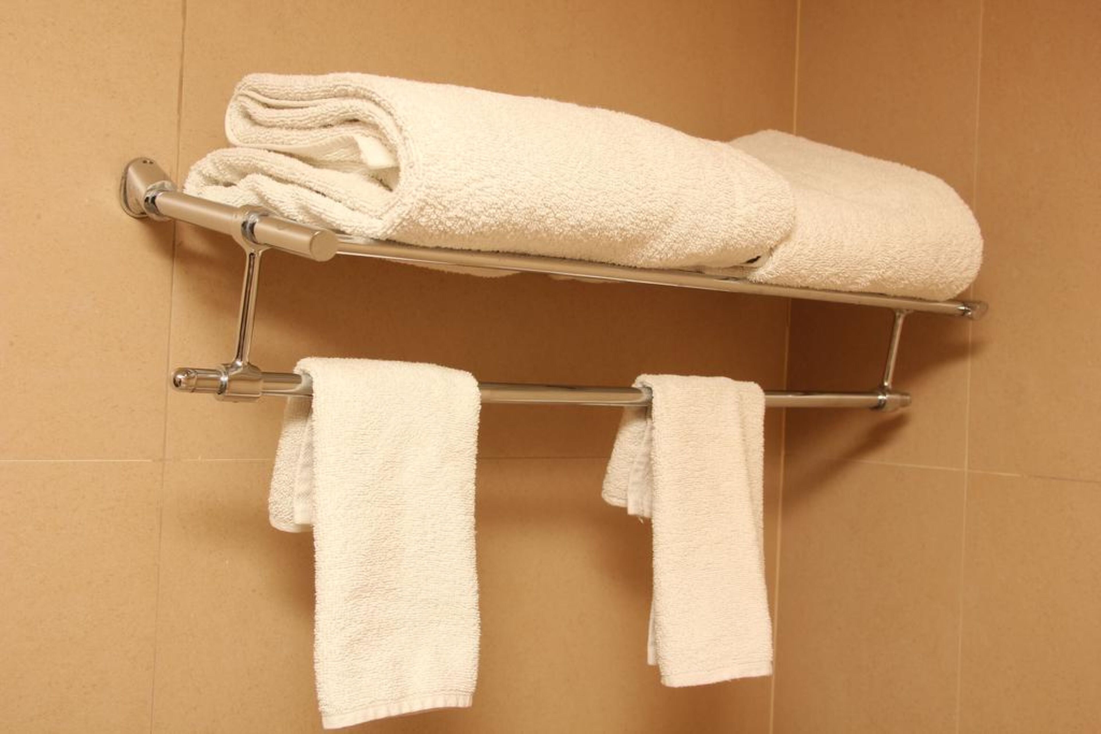 A bathroom with a towel rack holding two rolled towels and two hanging towels.