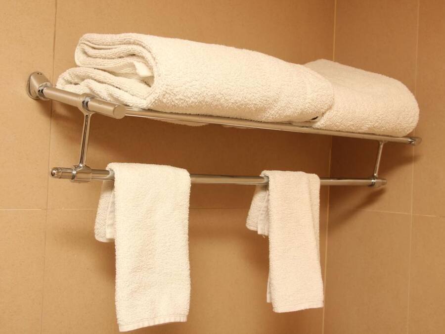 A bathroom with a towel rack holding two rolled towels and two hanging towels.
