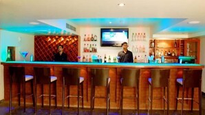 A bar area with a long counter, multiple stools, and a television screen above. - The Aures (Chhatrapati Sambhajinagar)