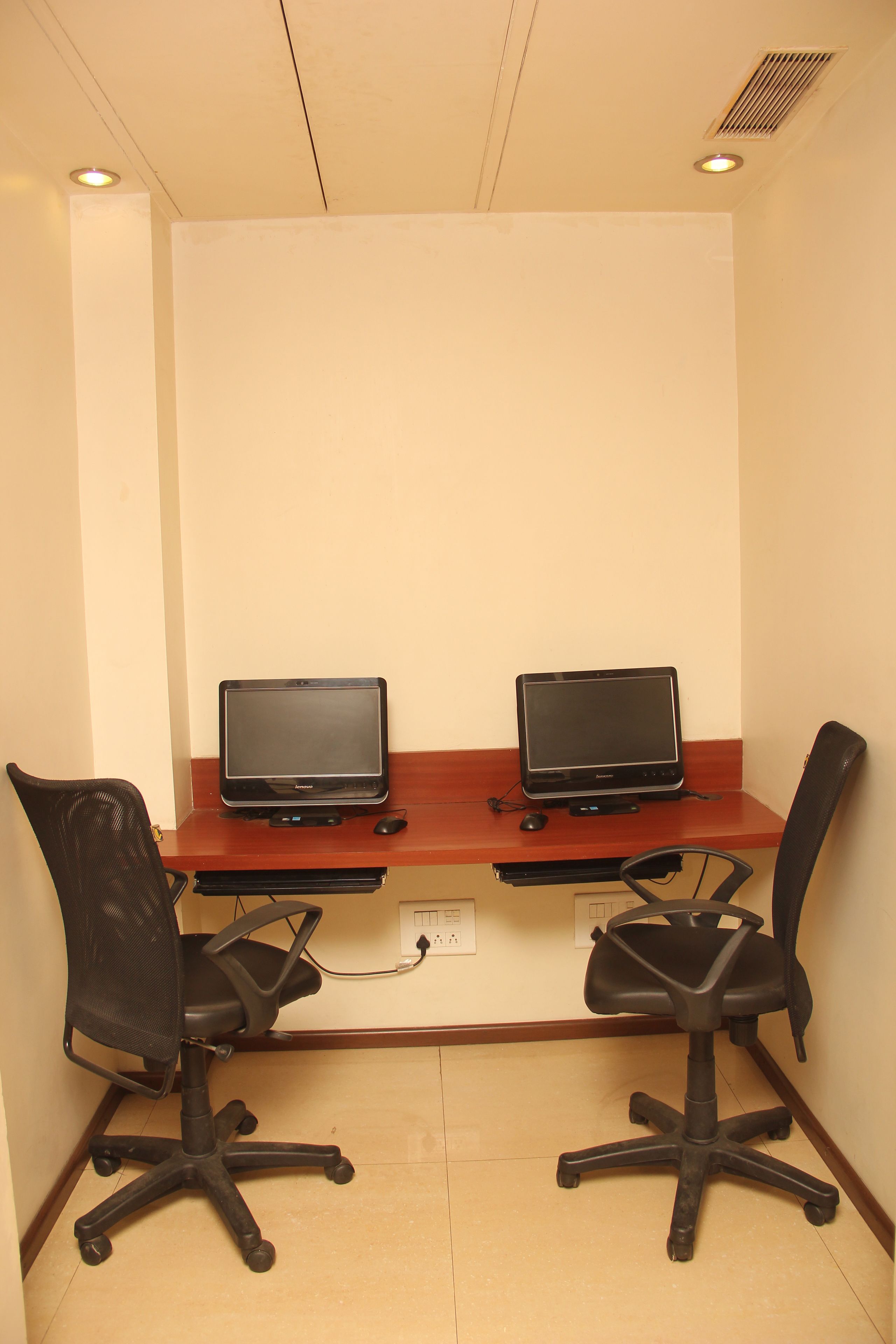 Un espacio de trabajo con dos portátiles sobre un escritorio de madera, dos sillas de oficina negras y un enchufe en la pared.