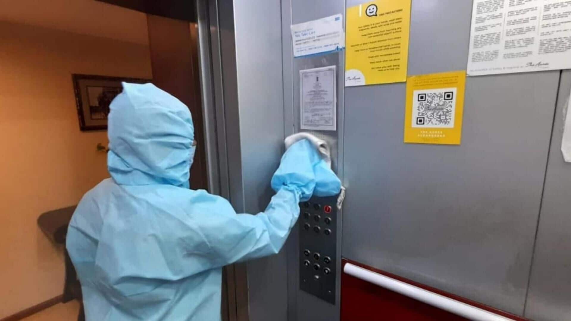 Una persona con traje azul de protección operando un panel de control de ascensor que incluye un código QR y avisos informativos.