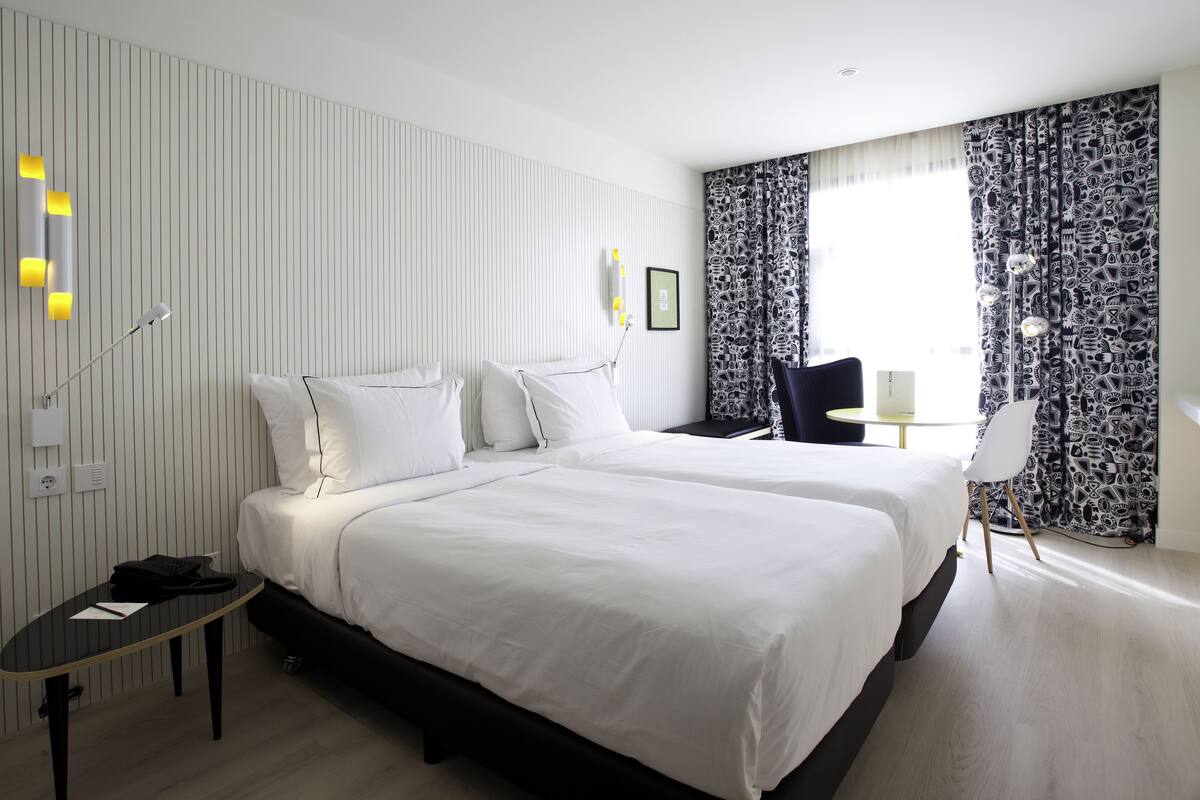 Hotellihuone, jossa on kaksi sänkyä, työpöytä ja tuoli.