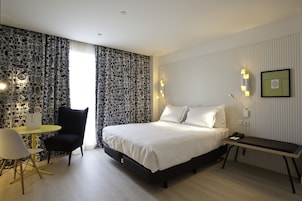 Une chambre d’hôtel moderne avec un grand lit, un bureau, une chaise et un mur décoré d’un motif.