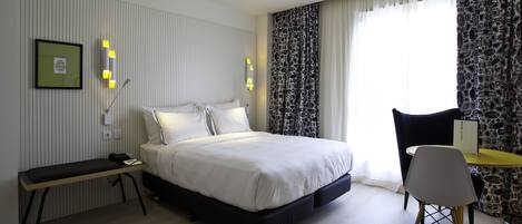 Una habitación de hotel moderna con una cama grande, una mesita de noche y un escritorio con una silla.