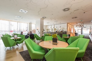 A modern interior with green chairs and tables, a bar area, and large windows.