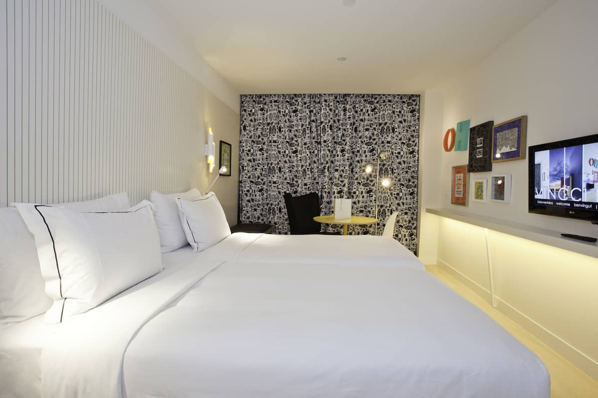 Hotellihuone, jossa on suuri sänky, pieni pöytä, televisio ja kuviollinen seinä.