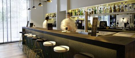 A modern bar with a long counter, multiple stools, and a variety of bottles on shelves.