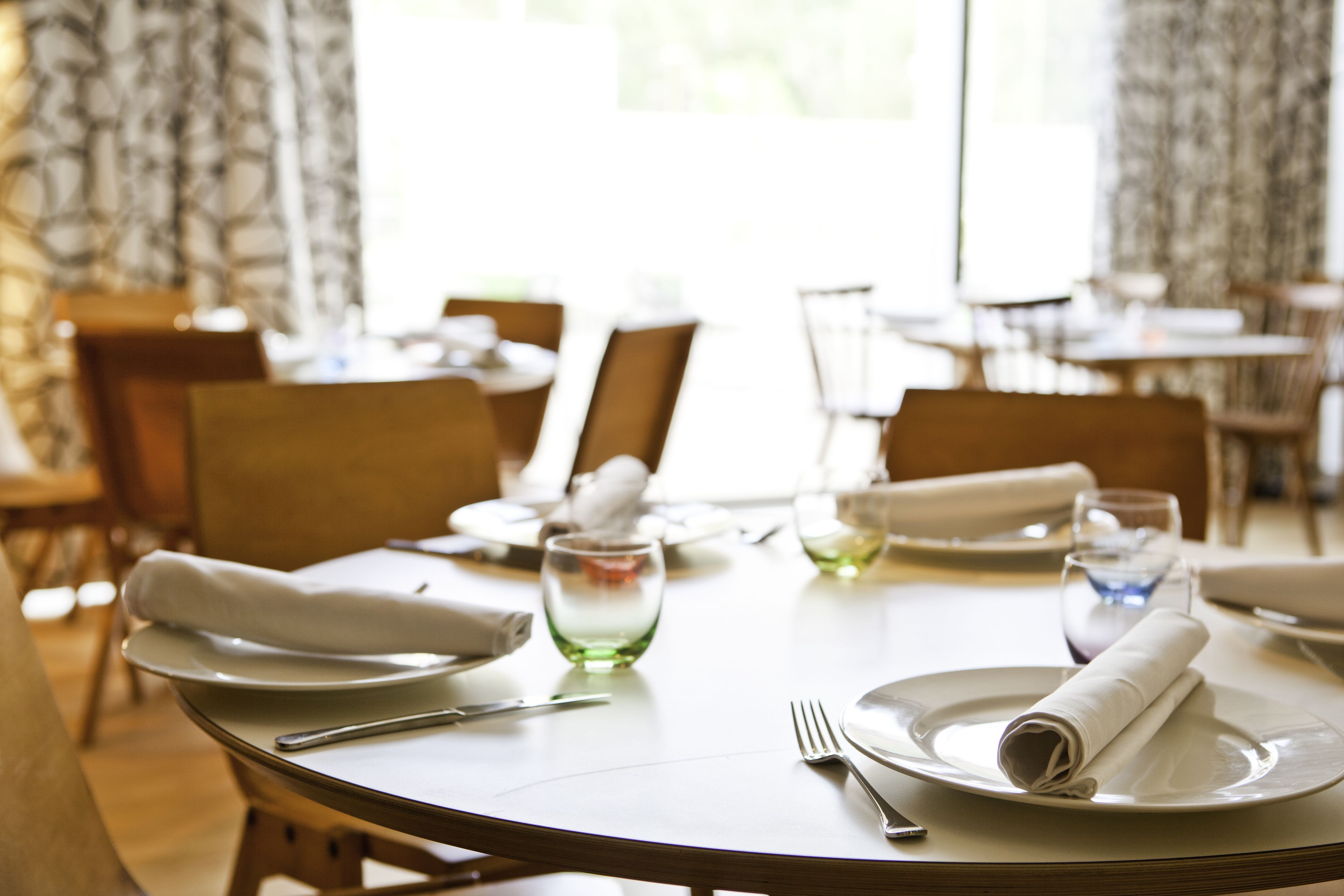 Un espace repas avec des tables rondes, des chaises et des tables soigneusement dressées, avec assiettes, verres et couverts.