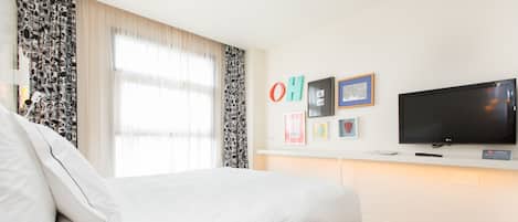 Une chambre d’hôtel moderne dotée d’un grand lit, d’un téléviseur à écran plat et d’une fenêtre avec des rideaux légers.