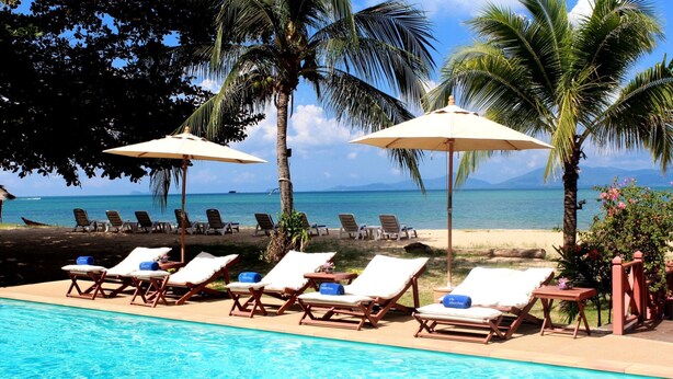 Zona junto a la piscina con sillones de descanso y sombrillas, con vista a una playa y al océano.