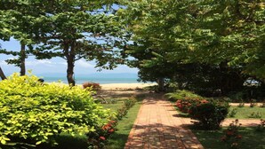 Un sendero pavimentado que conduce a una playa con exuberante vegetación y flores rojas.