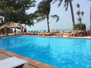 A poolside area with lounge chairs and a thatched-roof hut.