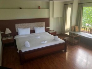 A well-furnished hotel room with a large bed, bedside tables, a small table, and a window with a view of greenery. - Chaweng Tara Hotel (Koh Samui)