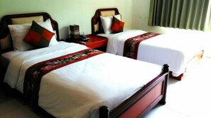 Two single beds with wooden frames and white bedding, each with a red and black patterned bedspread. There are two bedside tables with lamps, and a window with curtains. - Chaweng Tara Hotel (Koh Samui)