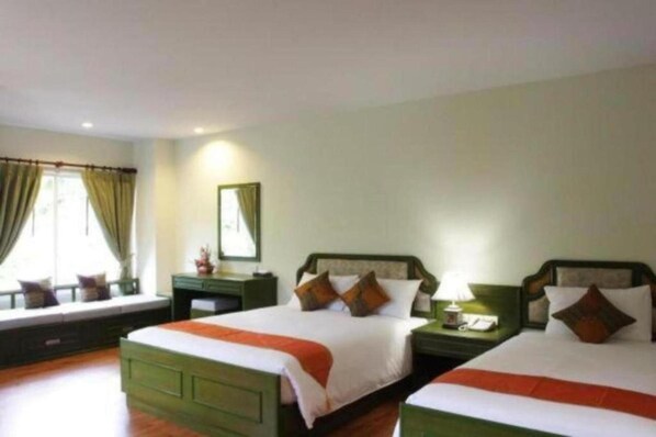 A hotel room with two beds, a window with curtains, a nightstand with a lamp, and a mirror on the wall. - Chaweng Tara Hotel (Koh Samui)