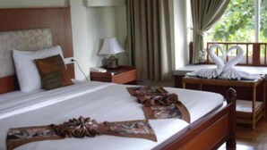 Una habitación de hotel con una cama grande, una mesita de noche, una lámpara y un ventanal con cortinas.