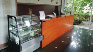 Un área de recepción con un mostrador de madera, una vitrina con productos alimenticios y vistas al exterior con vegetación.