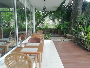 An outdoor seating area with tables and wicker chairs, surrounded by glass walls and potted plants. - Chaweng Tara Hotel (Koh Samui)