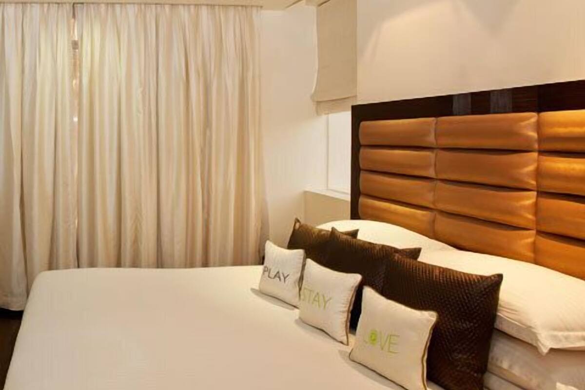 A hotel room with a large bed, beige curtains, and a headboard with a padded design.