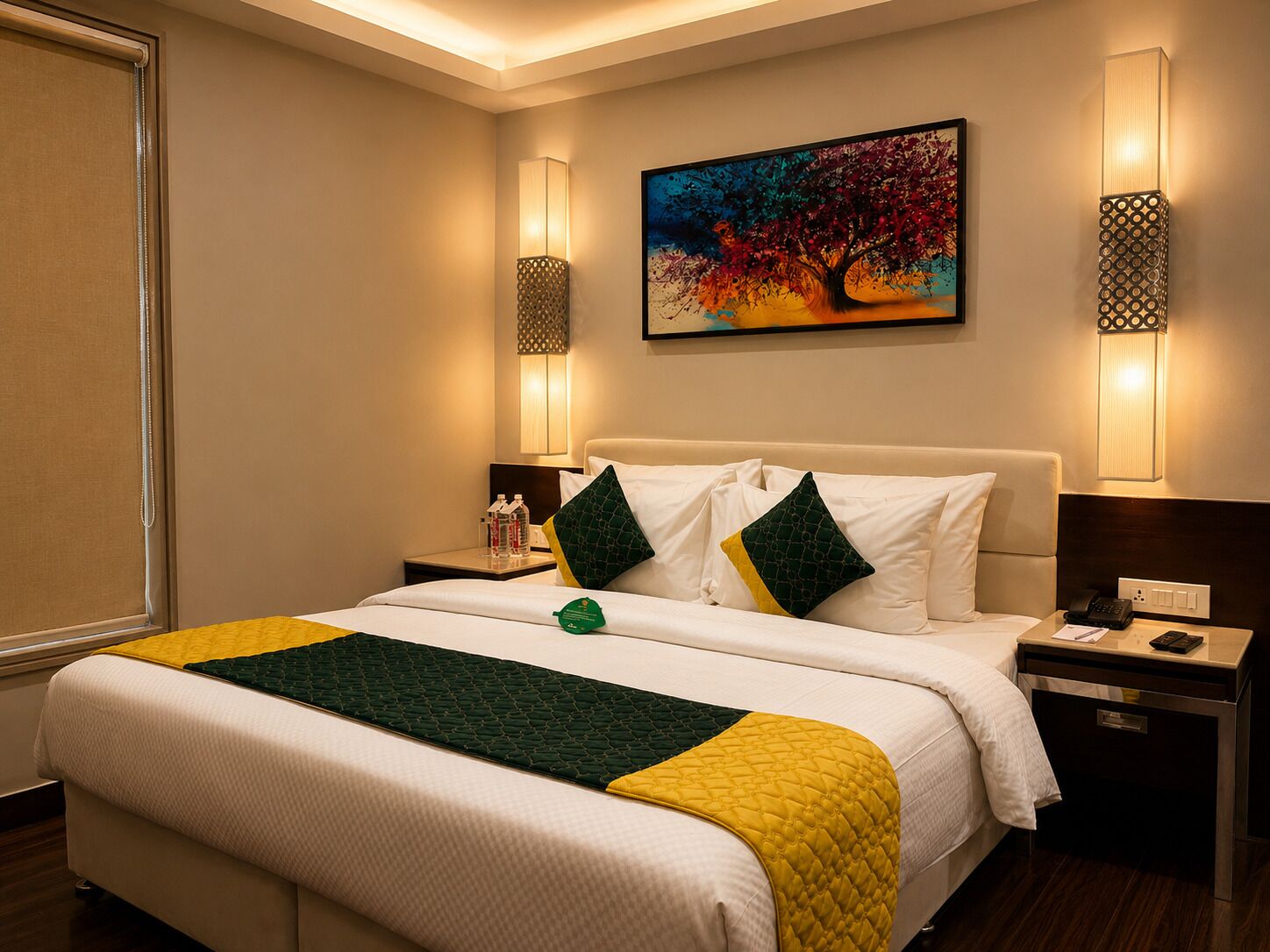 A hotel room with a bed, bedside tables, a painting, and wall sconces.