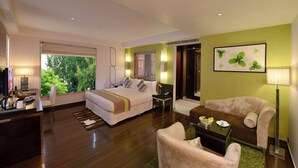 A hotel room with a bed, a desk with a lamp, a chair, a sofa, and a painting on the wall. - Quality Inn Gurgaon (Gurugram)