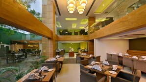 A modern dining area with multiple tables and chairs, a central buffet, and a view of the outdoor patio. - Quality Inn Gurgaon (Gurugram)