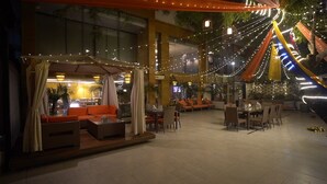 An outdoor seating area with tables and chairs, string lights, and draped fabric. - Quality Inn Gurgaon (Gurugram)
