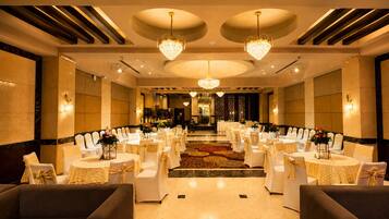 A banquet hall with round tables and chairs, chandeliers, and a carpeted floor.