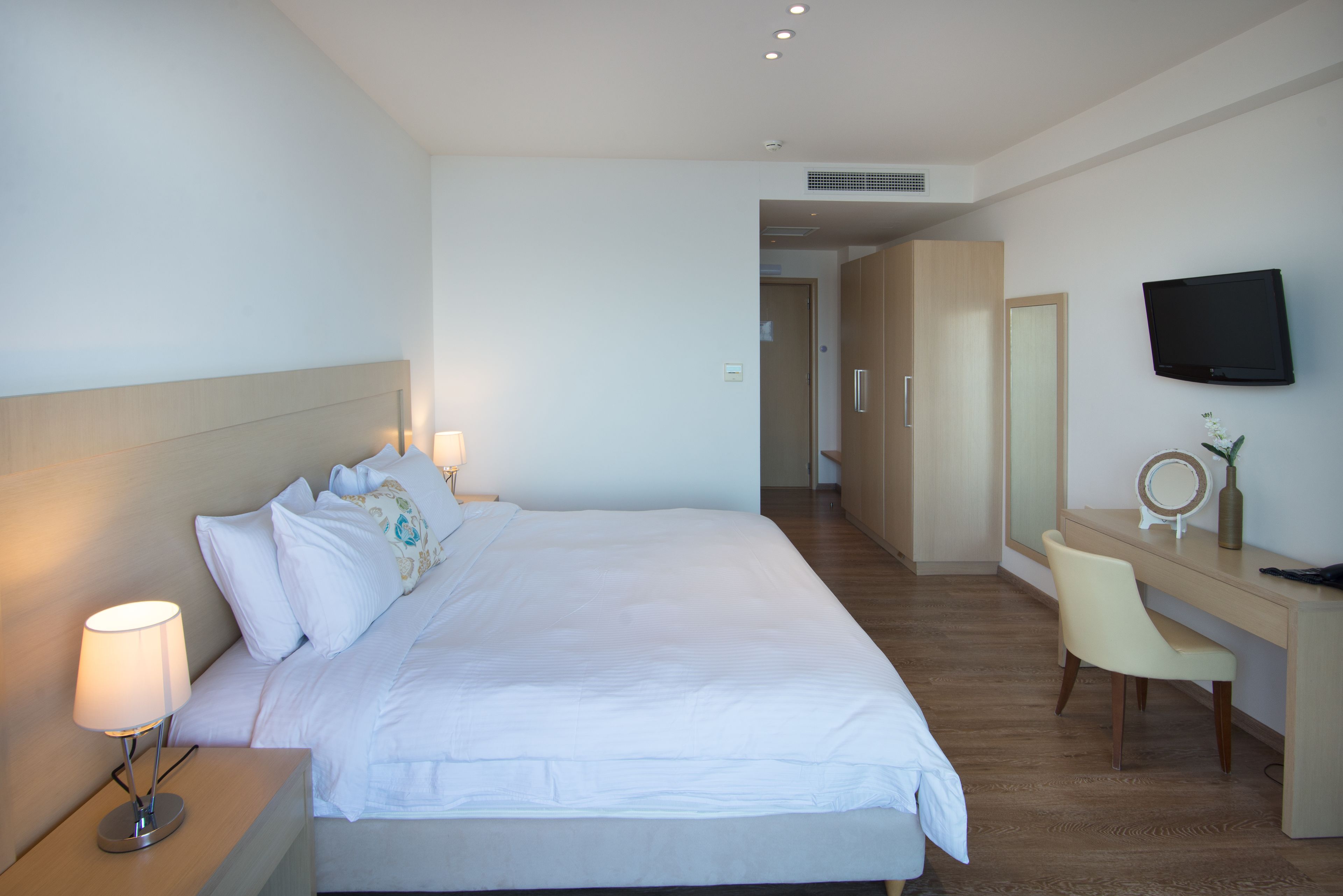 A hotel room with a large bed, bedside lamps, a desk with a chair, a TV, and a mirror.