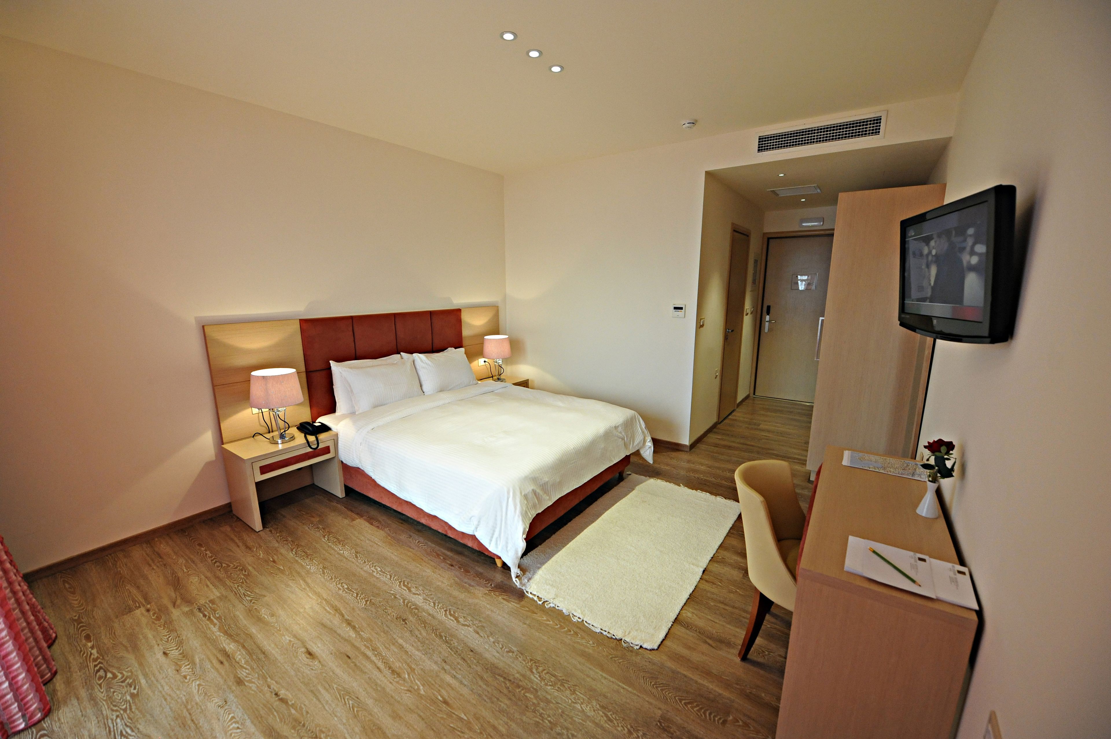 A hotel room with a bed, bedside tables, a desk, a chair, and a television.