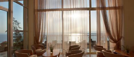 A spacious room with large windows, a dining area with chairs and a table, and a view of the sea.