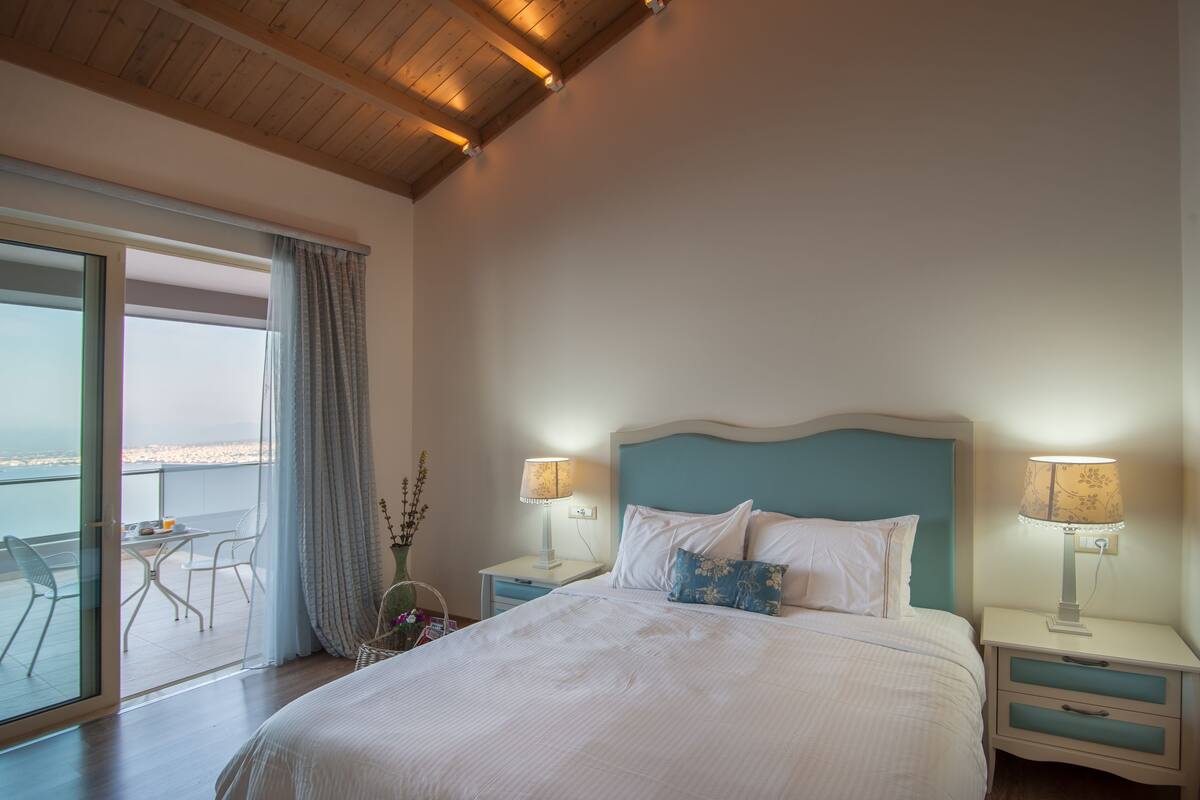 Une chambre à coucher avec un lit, deux tables de chevet avec des lampes, une fenêtre avec des rideaux et une vue sur l’extérieur.