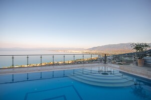 Uma piscina com vista para uma cidade costeira e montanhas ao fundo.