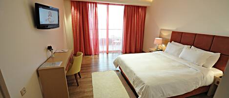 Habitación de hotel con cama, escritorio, silla, televisor y ventana con cortinas.