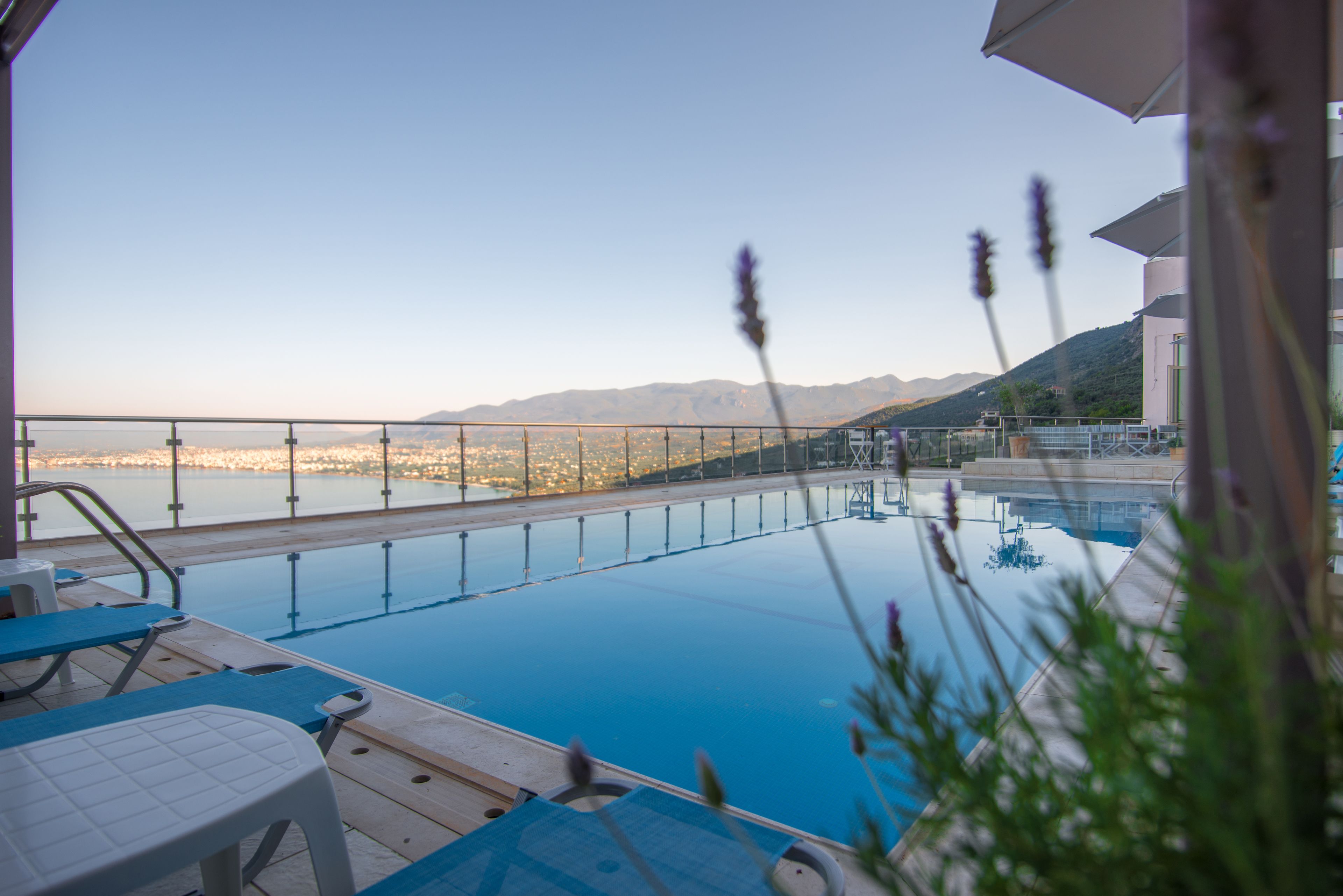 An outdoor swimming pool with lounge chairs and a view of a cityscape and mountains in the background.