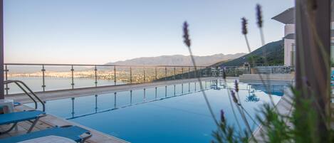 An outdoor swimming pool with lounge chairs and a view of a cityscape and mountains in the background.