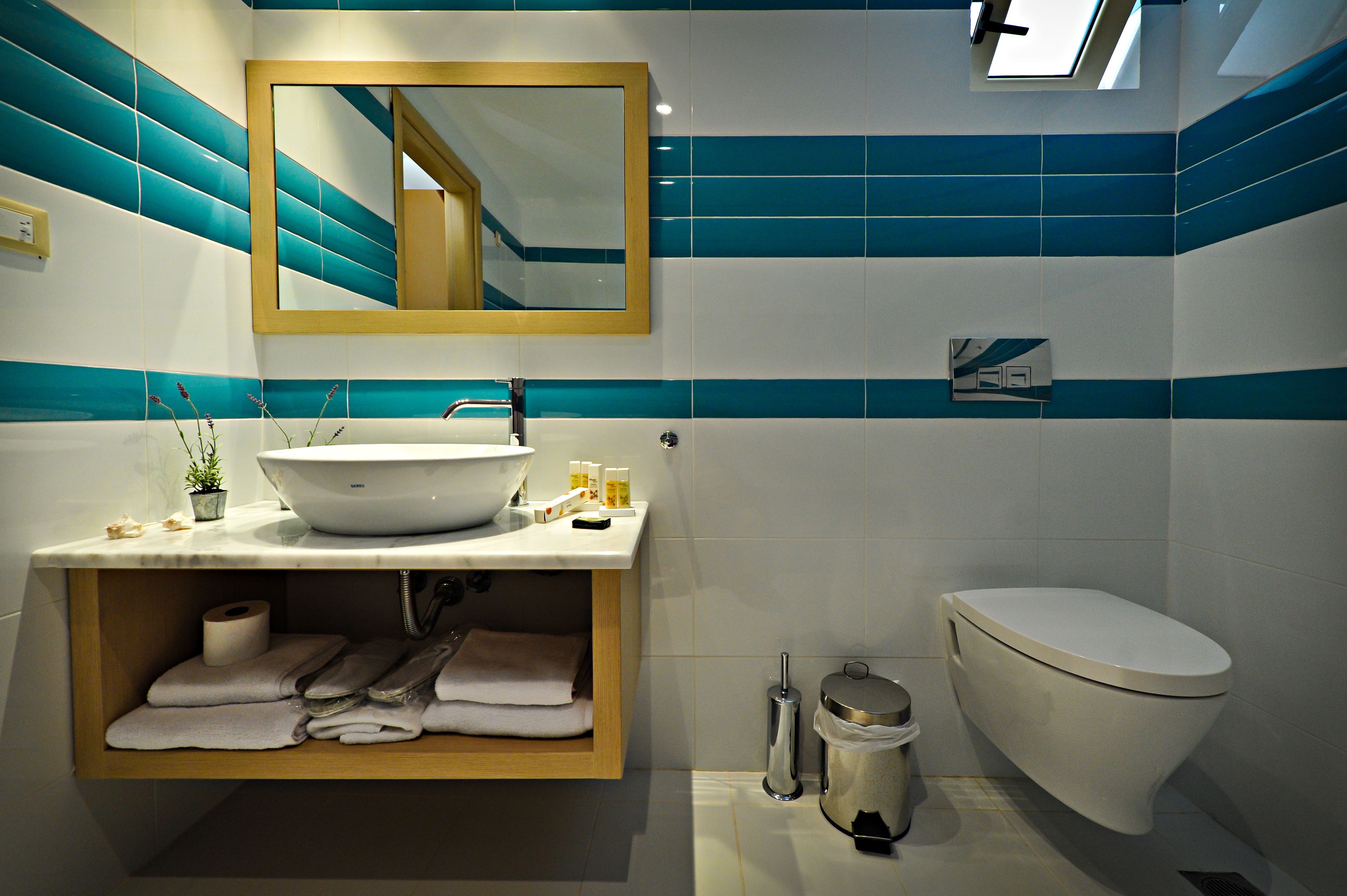A bathroom with a white sink, a mirror, a toilet, and a shelf with towels.