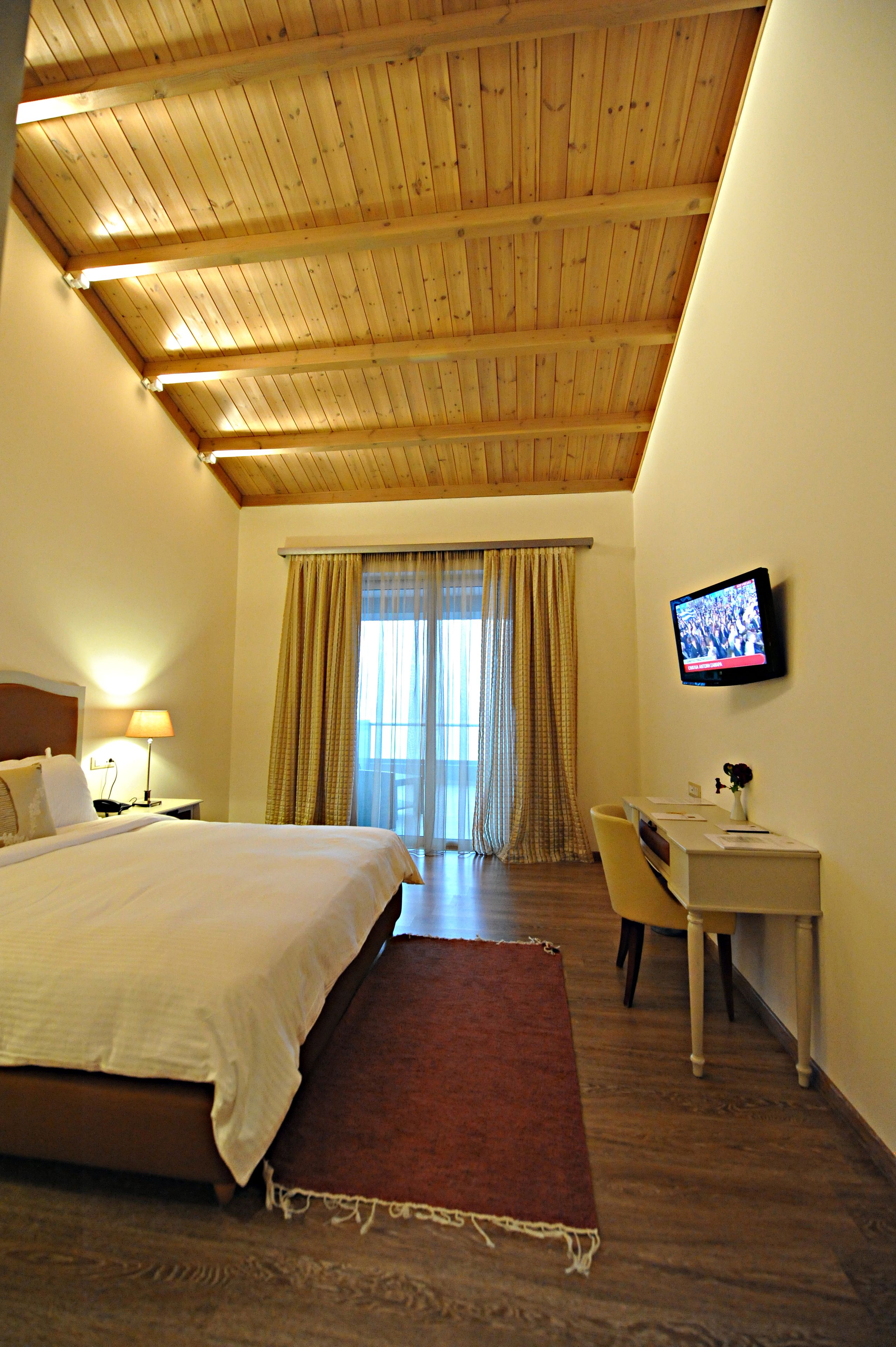 Una camera d'albergo con soffitto in legno, un letto, una scrivania, una sedia, un televisore e una finestra con tende.
