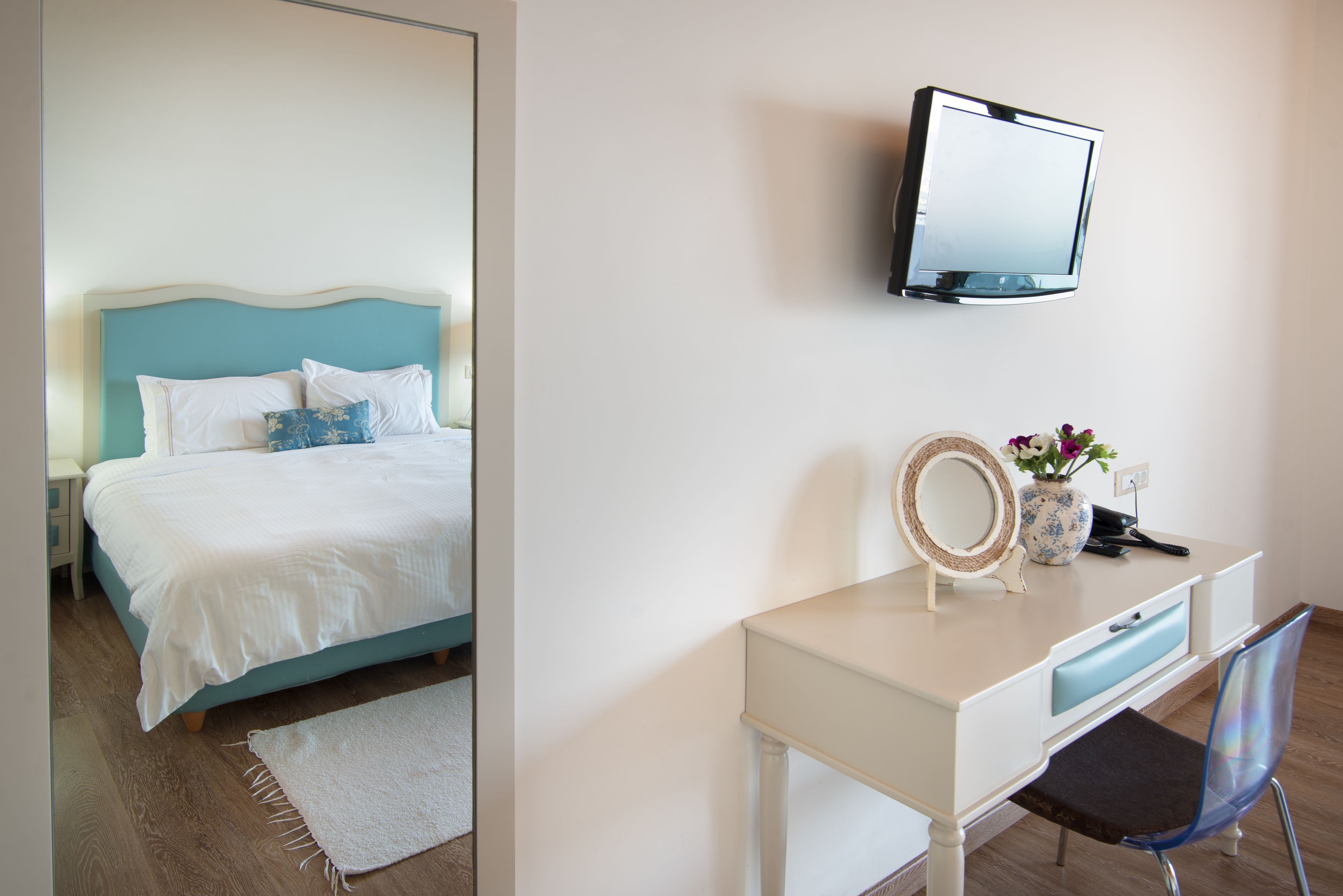 A bedroom with a bed, a bedside table, a dresser, a mirror, and a television on the wall.