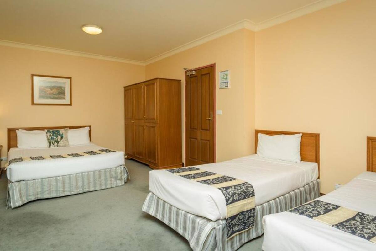 A hotel room with two beds, a wardrobe, a nightstand, and a framed picture on the wall.