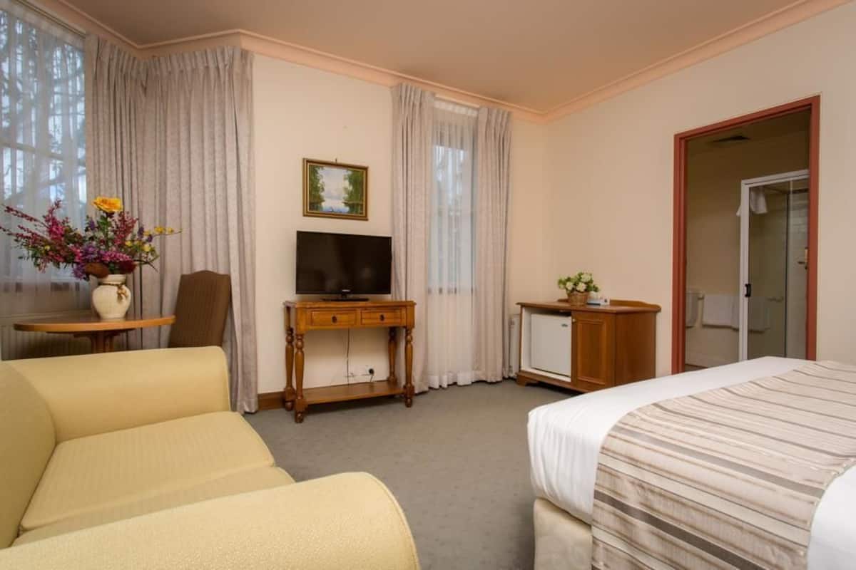 A hotel room with a bed, a desk with a television, a chair, and a small cabinet.