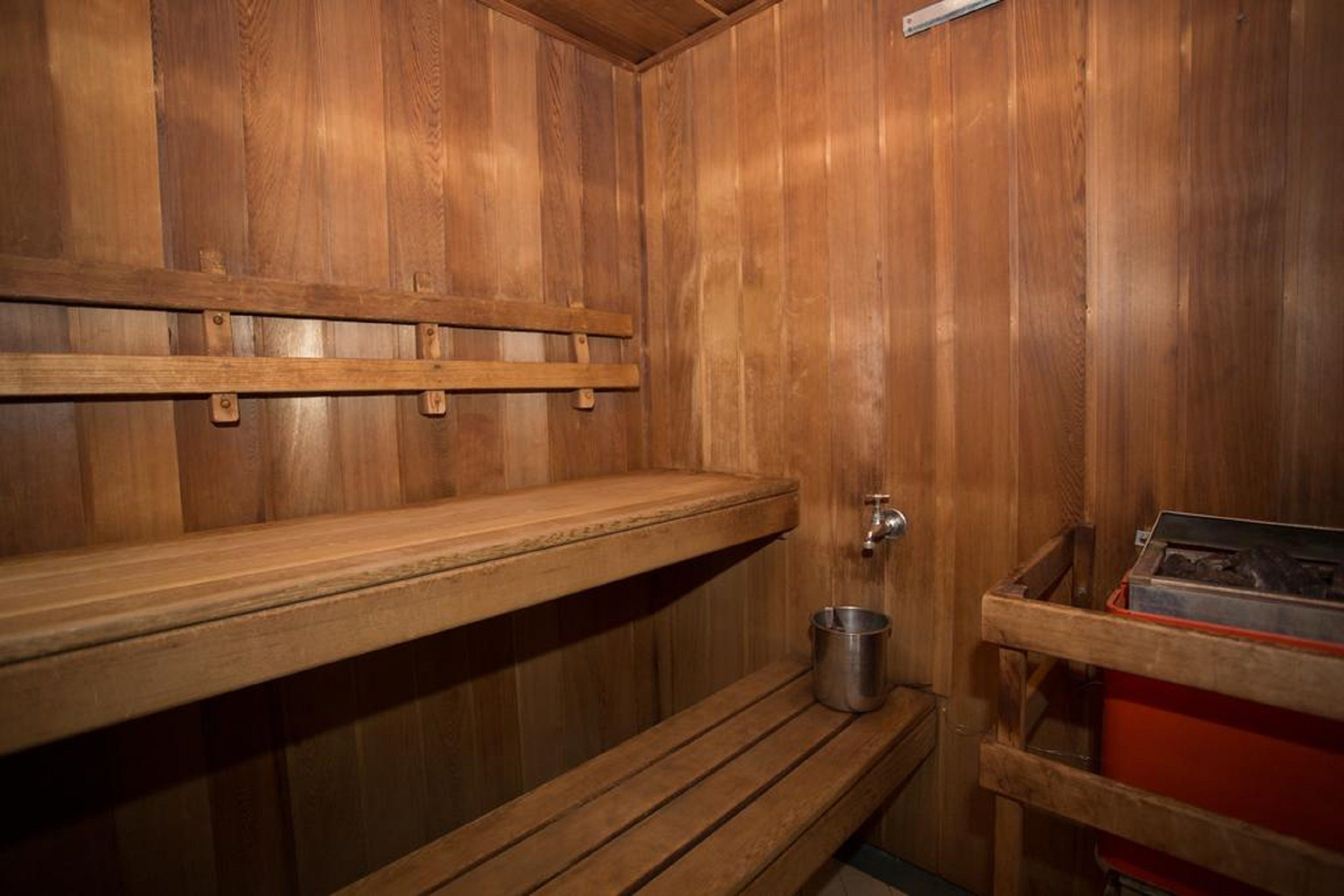 A wooden sauna with benches, a metal bucket, and a red storage unit.