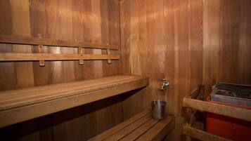 A wooden sauna with benches, a metal bucket, and a red storage unit.