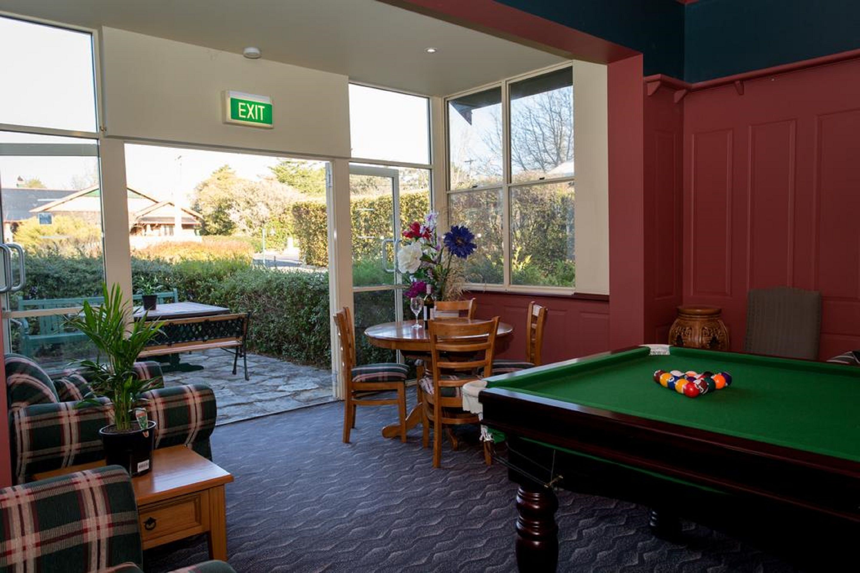 A billiards table with balls, a green sofa, a dining table with chairs, and a vase with flowers.