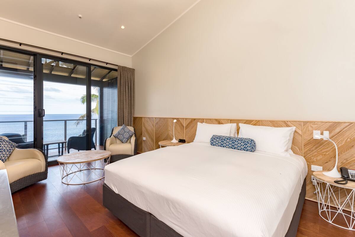 A spacious bedroom with a large bed, a seating area with a table, and a view of the ocean.
