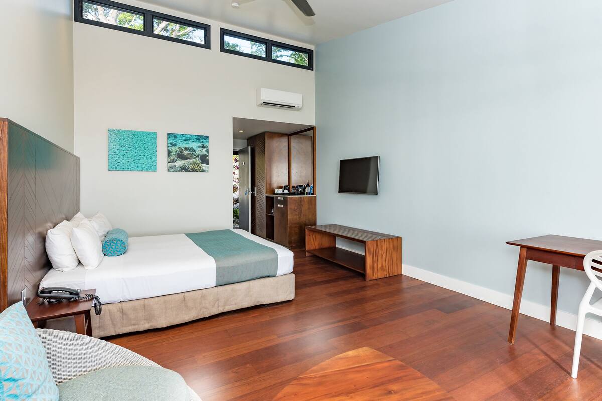 A modern hotel room with a bed, a desk, a chair, a TV, and artwork on the wall.