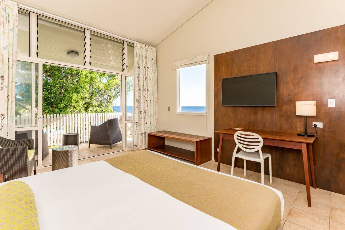 A hotel room with a bed, a desk, a chair, a TV, and a view of the outdoors.