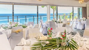 A restaurant with tables set for dining, large windows with a view of the ocean, and a ceiling fan. - Scenic Matavai Resort Niue (Tamakautoga)